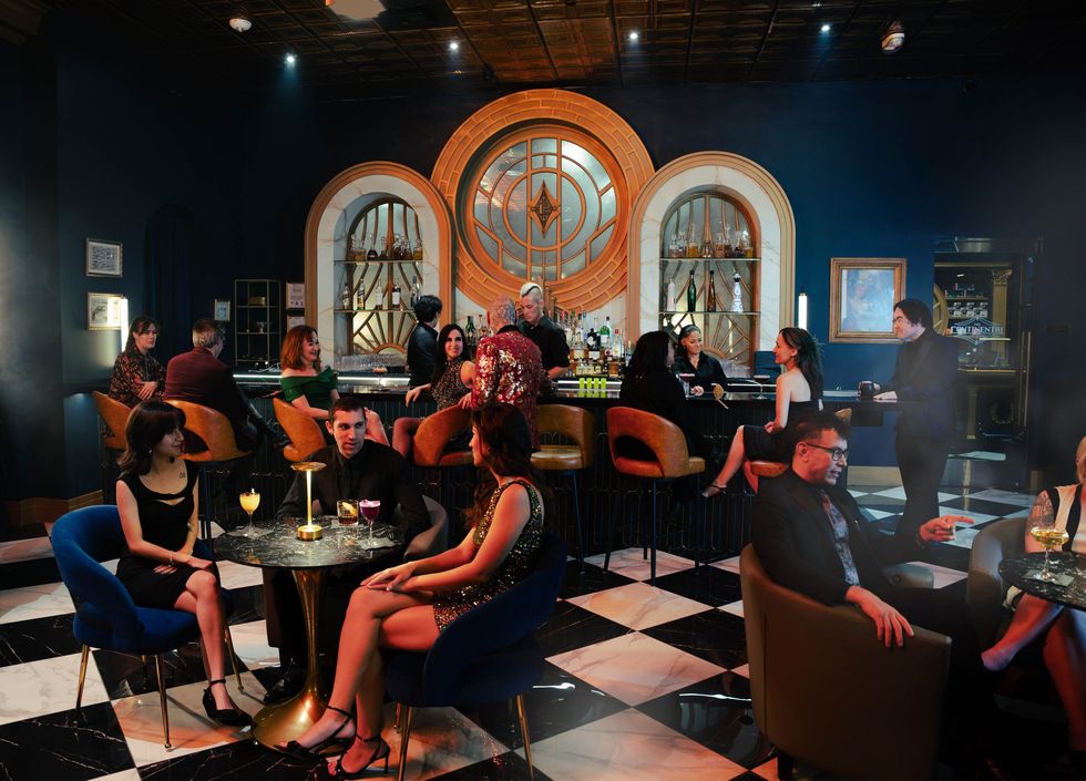 Elegant bar with patrons in evening attire, black and white floor, and art deco decor.
