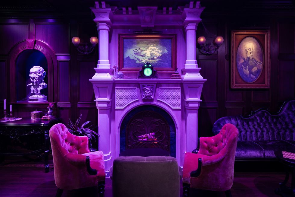 Elegant, dimly lit room with purple chairs, ornate fireplace, and eclectic artwork.