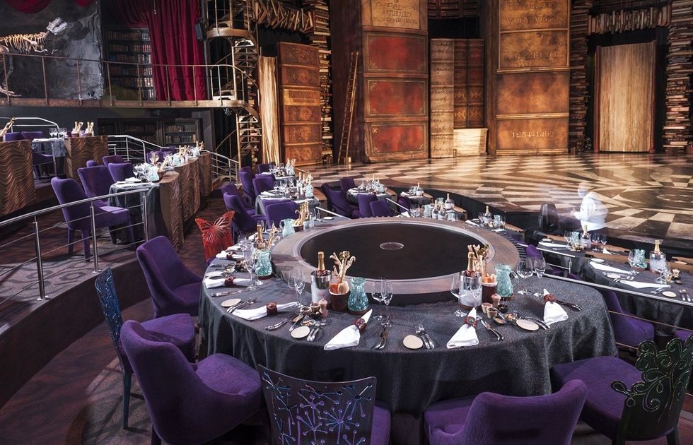 Elegant dining area with purple chairs and large stage set in a theatrical venue.