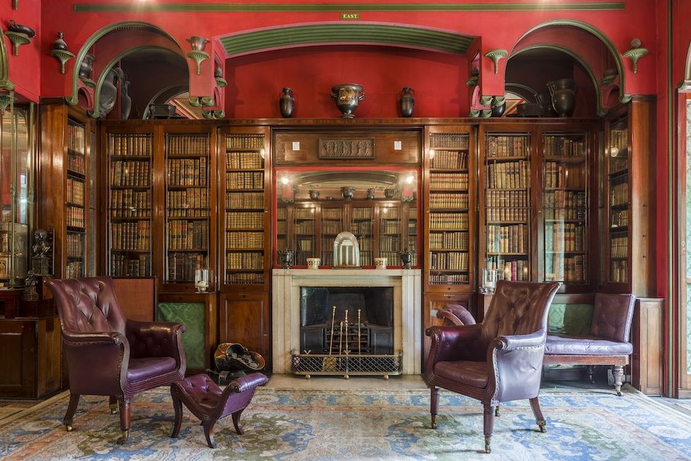 Elegant library with red walls, leather chairs, fireplace, and bookshelves filled with books.