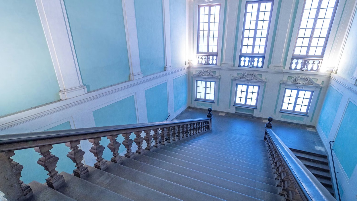 Elegant staircase at Uffizi Galleries with blue walls and large windows in a grand interior.