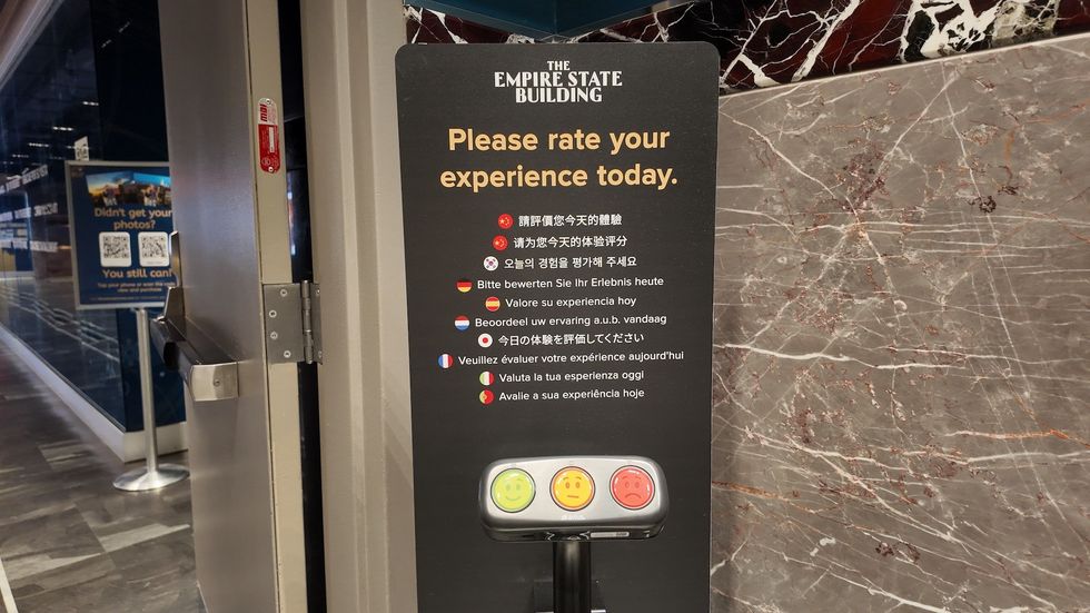 Empire State Building feedback station with multilingual instructions and emoji buttons.