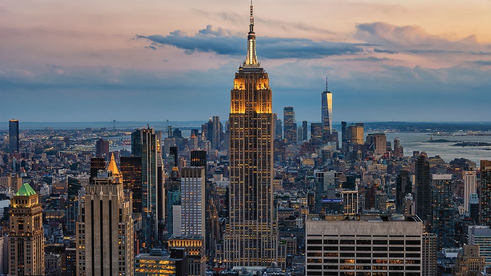 Empire State Building glowing at dusk with city skyline in the background.