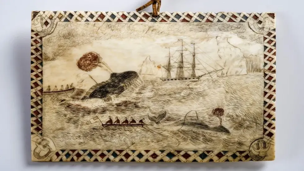 Engraved whaling scene on whale bone depicts boats, whales, and a ship at sea with a patterned border.