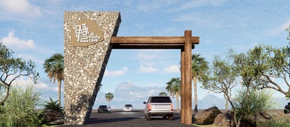 Entrance archway to Al Hoota Cave with cars and greenery under a clear sky.
