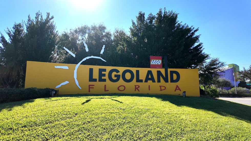 Entrance sign for Legoland Florida with sun graphic and lush green lawn.