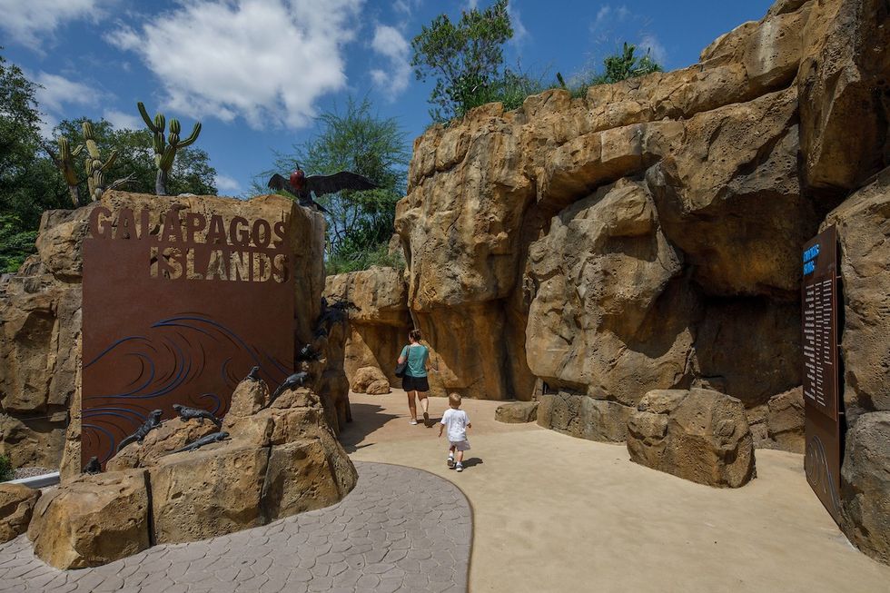 Entrance to Galapagos Islands exhibit with rocks and cactus, man and child walking inside.