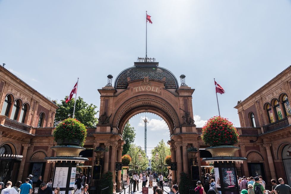 Entrance to Tivoli Gardens in Copenhagen, with flags and visitors walking through.