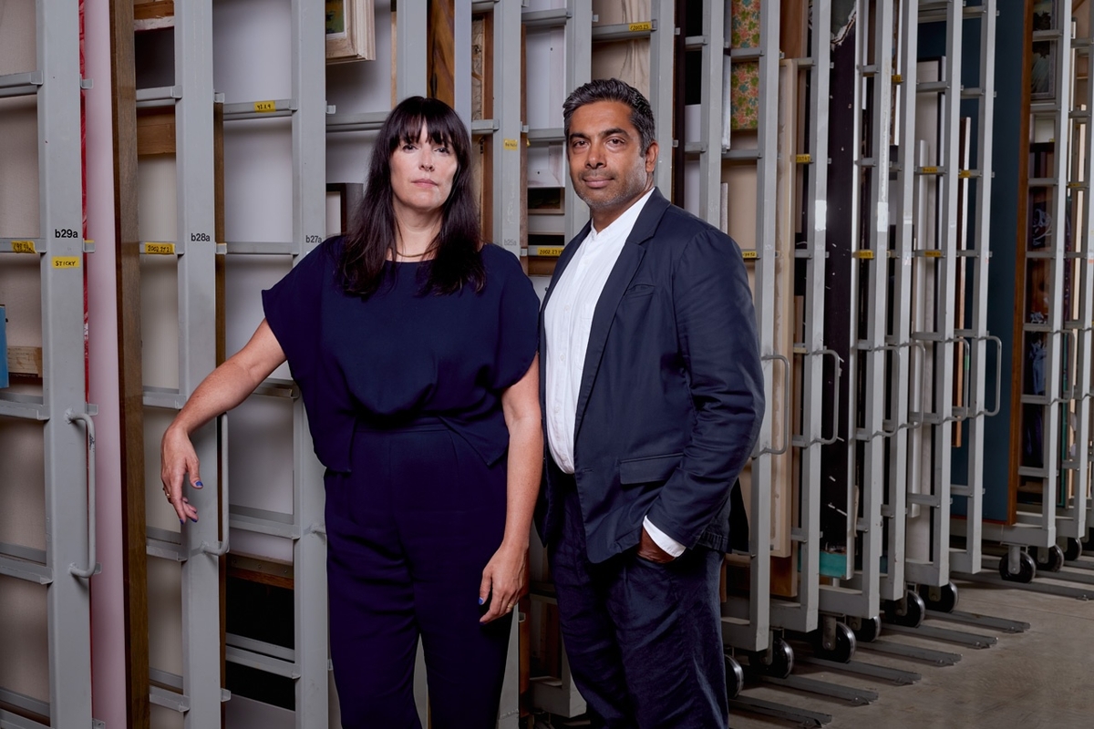 Eva Respini and Sirish Rao in formal attire standing in an art storage room with large shelves behind.