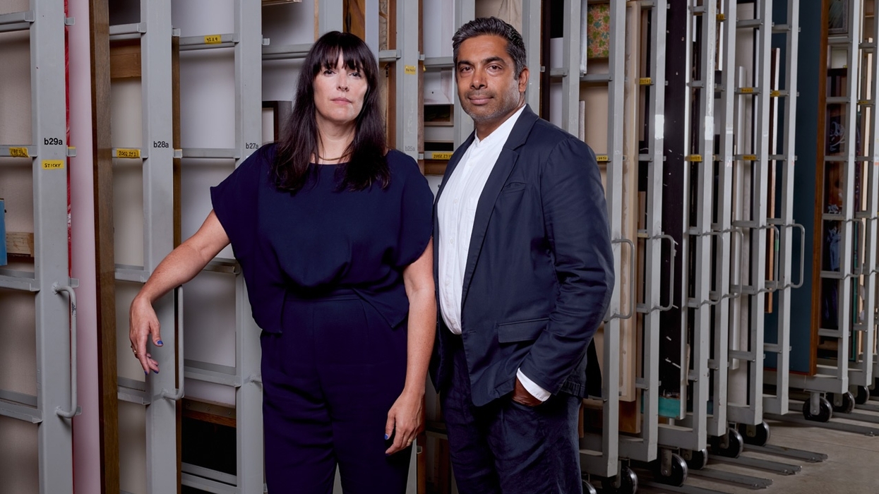 Eva Respini and Sirish Rao in formal attire standing in an art storage room with large shelves behind.