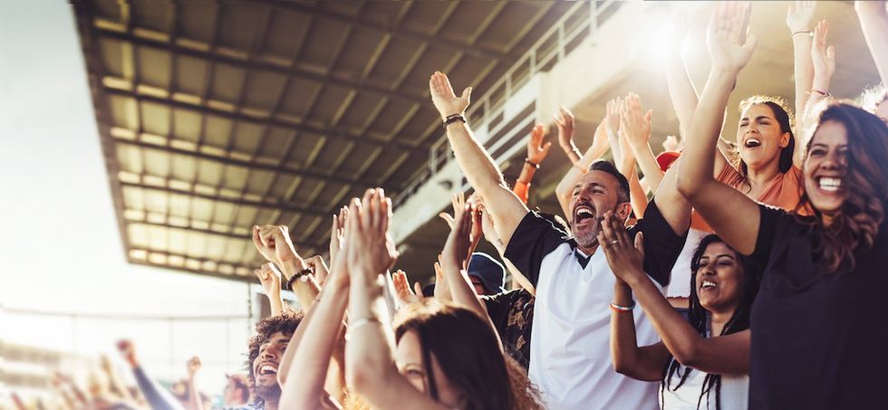 Excited fans in a stadium cheering with arms raised.