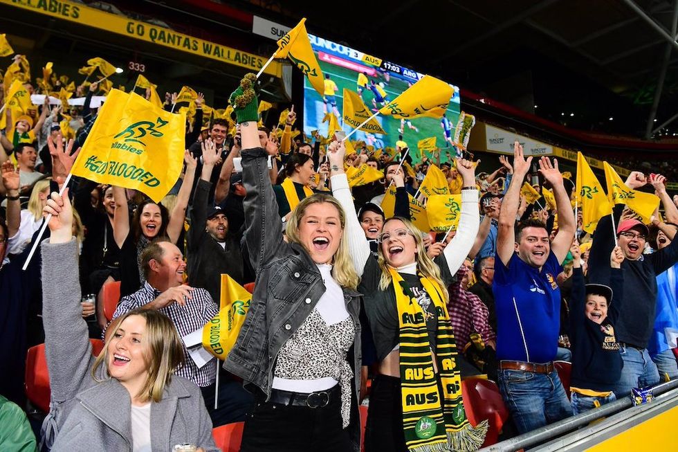 Excited rugby fans waving yellow flags in a crowded stadium.