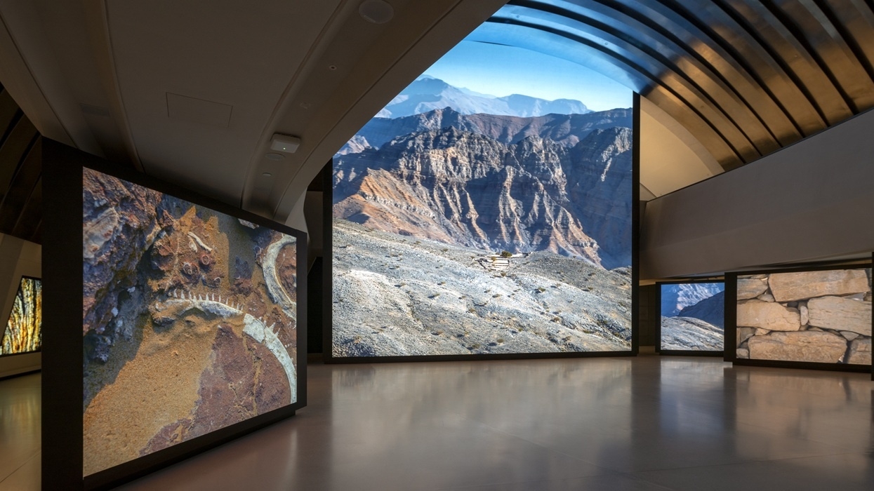 Exhibit at Zayed National Museum with large digital displays of rugged landscapes and geological formations.