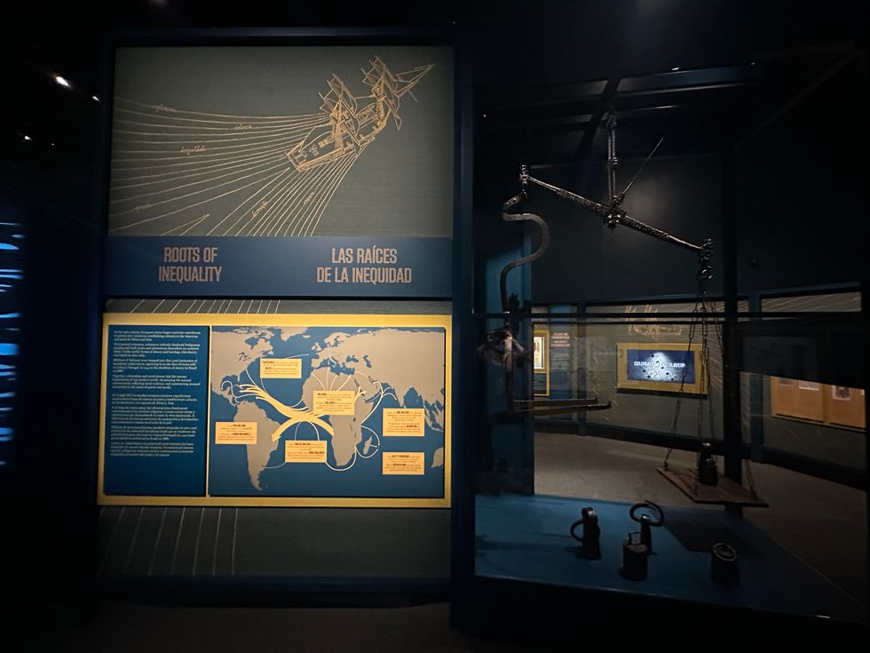 Exhibit on inequality's roots, featuring maps and historical objects in a dimly lit setting.