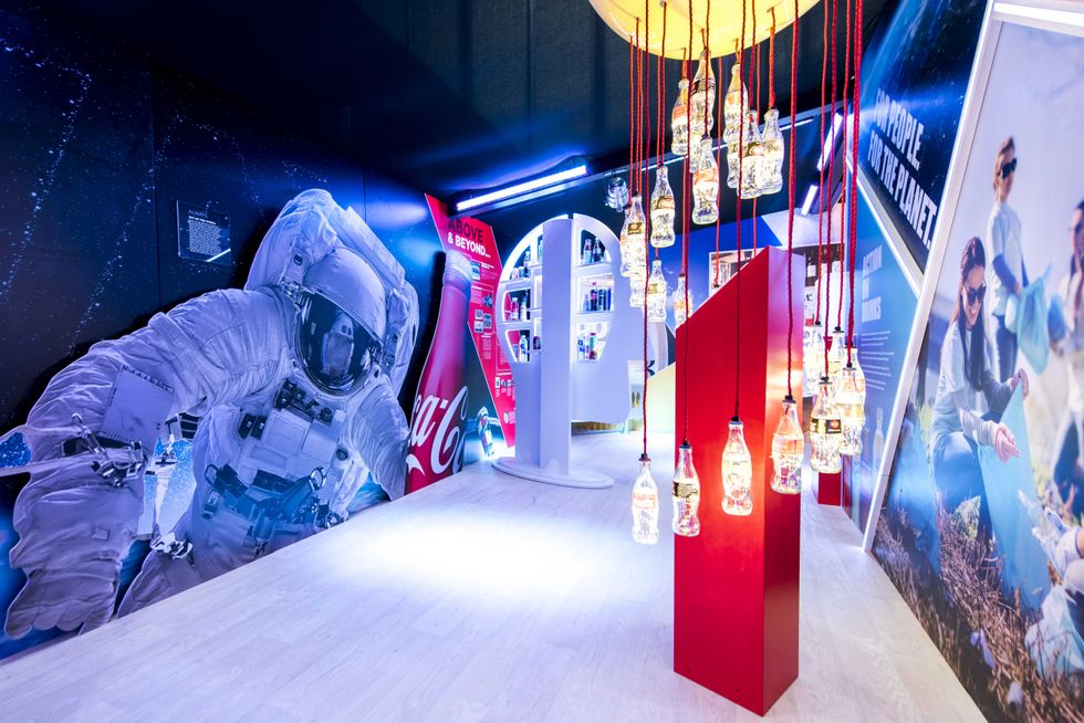 Exhibit with astronaut cutout, hanging bottles, and Coca-Cola branding in bright lighting.
