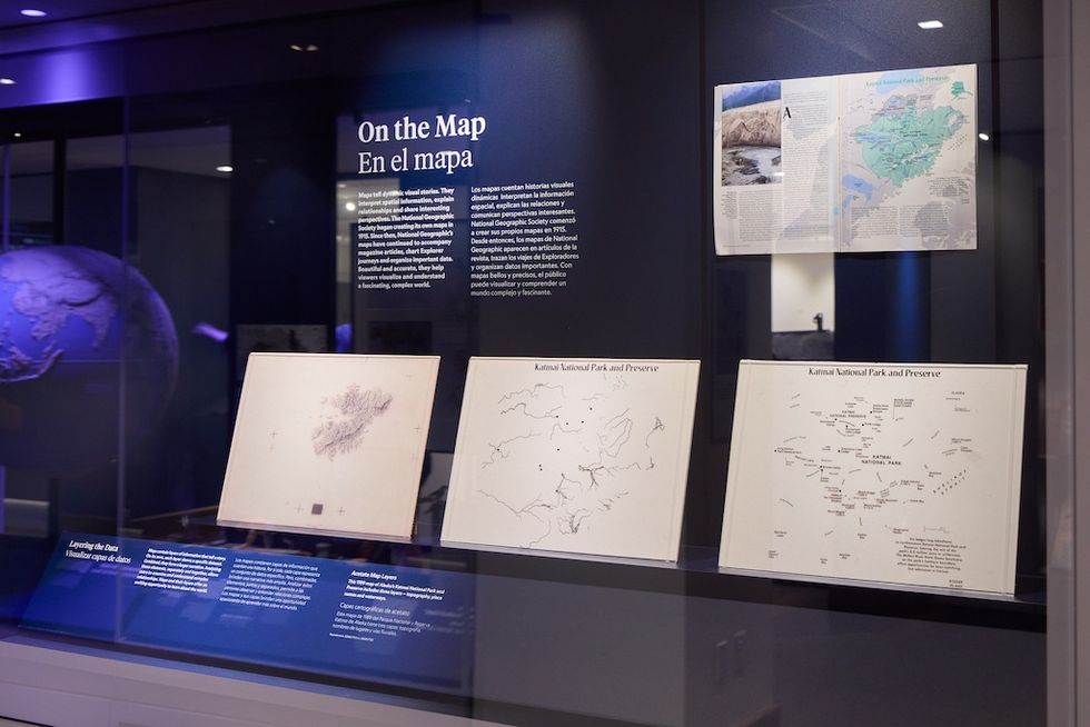 Exhibit with historical maps and text, "On the Map/En el mapa," in a dimly lit room.