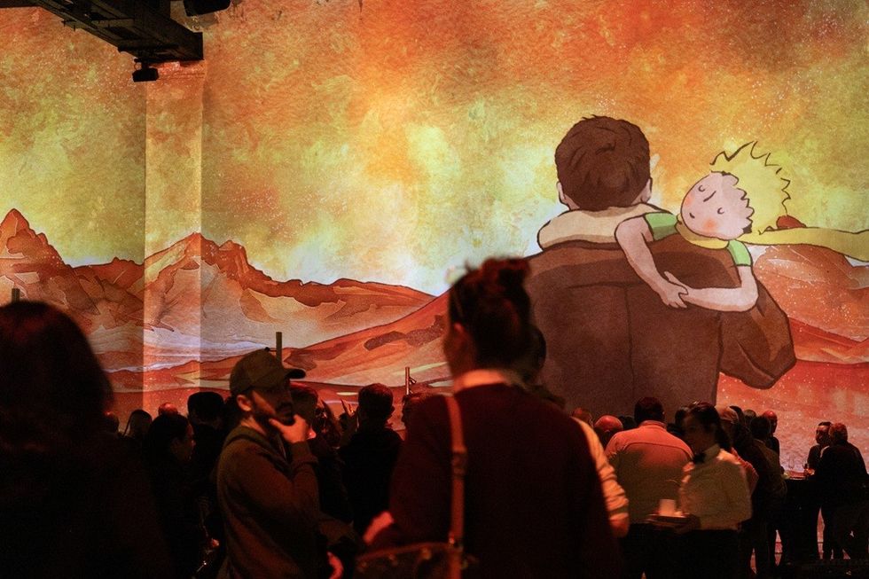 Exhibit with projected illustration of a boy on a man's shoulder; crowd observing.