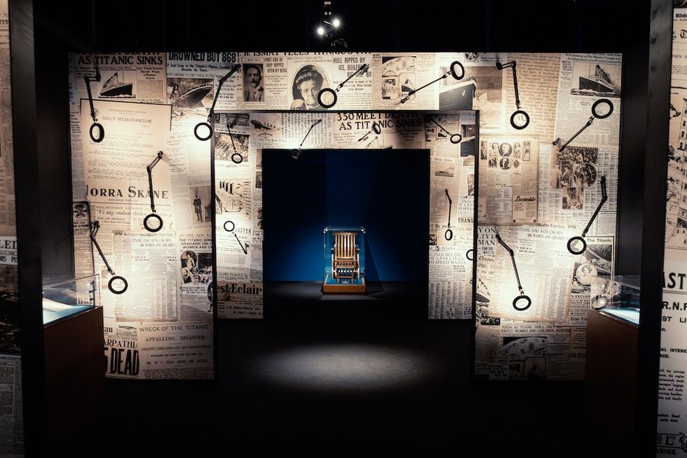 Exhibit with Titanic newspaper clippings and a central wooden chair on display.