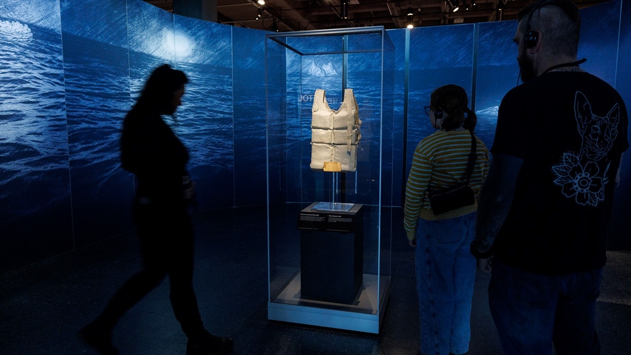 Exhibition visitors view a vintage life jacket in a glass case against a watery backdrop in Titanic: The Human Story