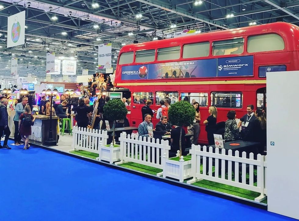 Exhibition with a red double-decker bus booth surrounded by attendees and displays.