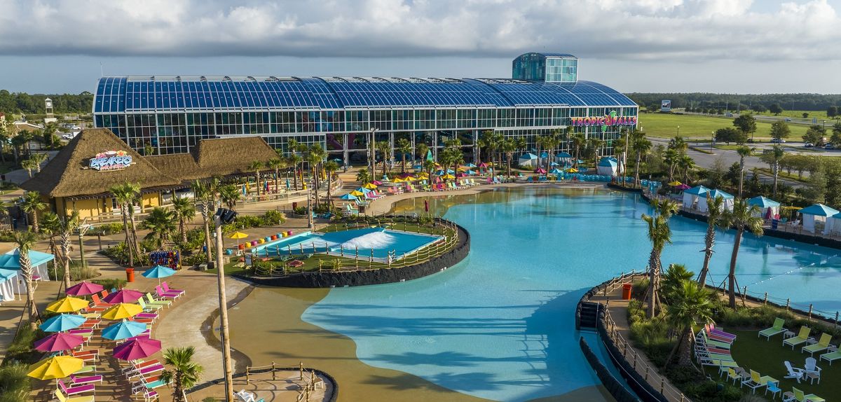 Expansive water park with pools, slides, colorful umbrellas, and a glass-roofed building.