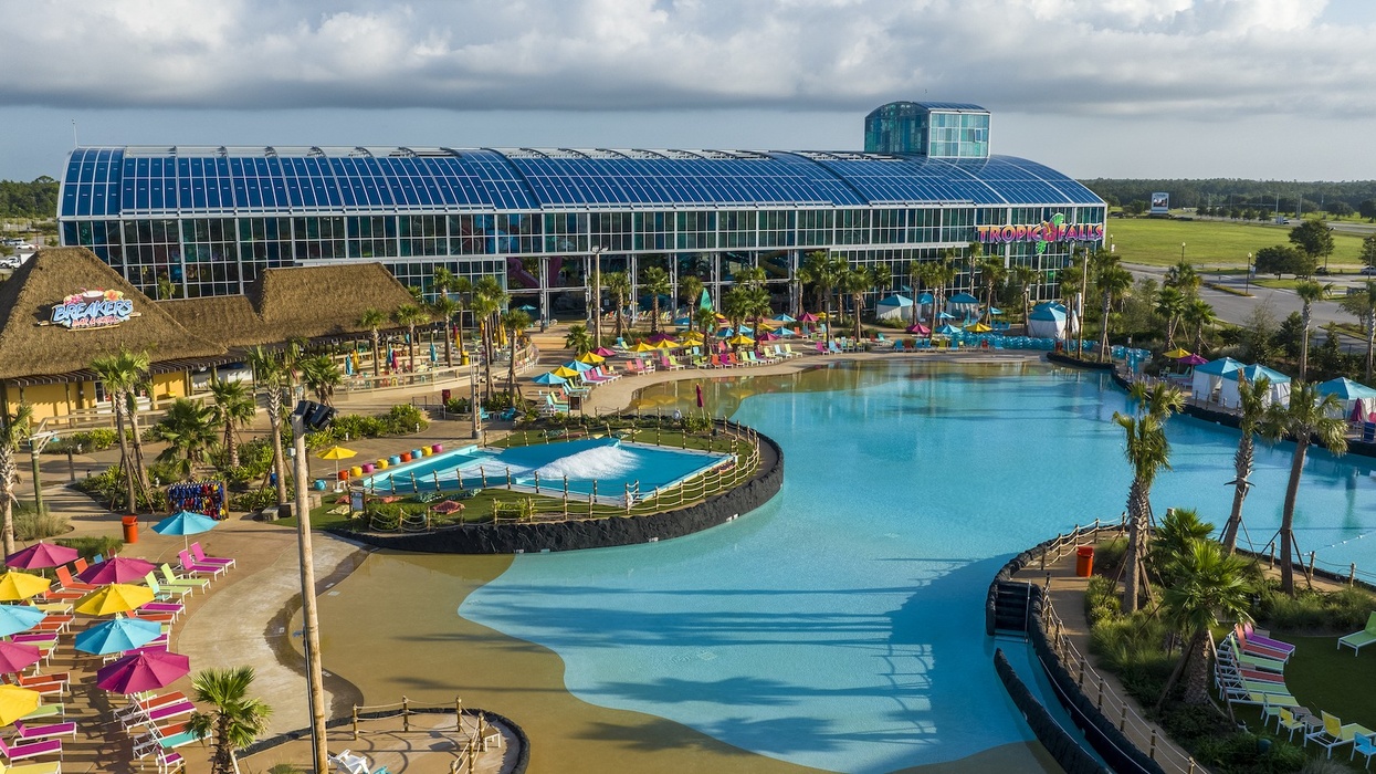 Expansive water park with pools, slides, colorful umbrellas, and a glass-roofed building.