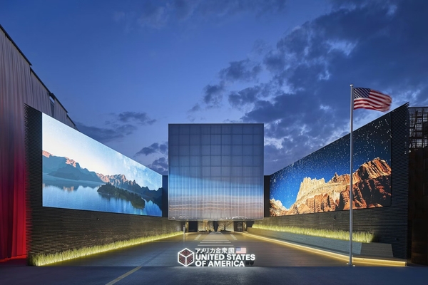 Expo Osaka 2025 US pavilion with large landscape displays and a waving flag at dusk.