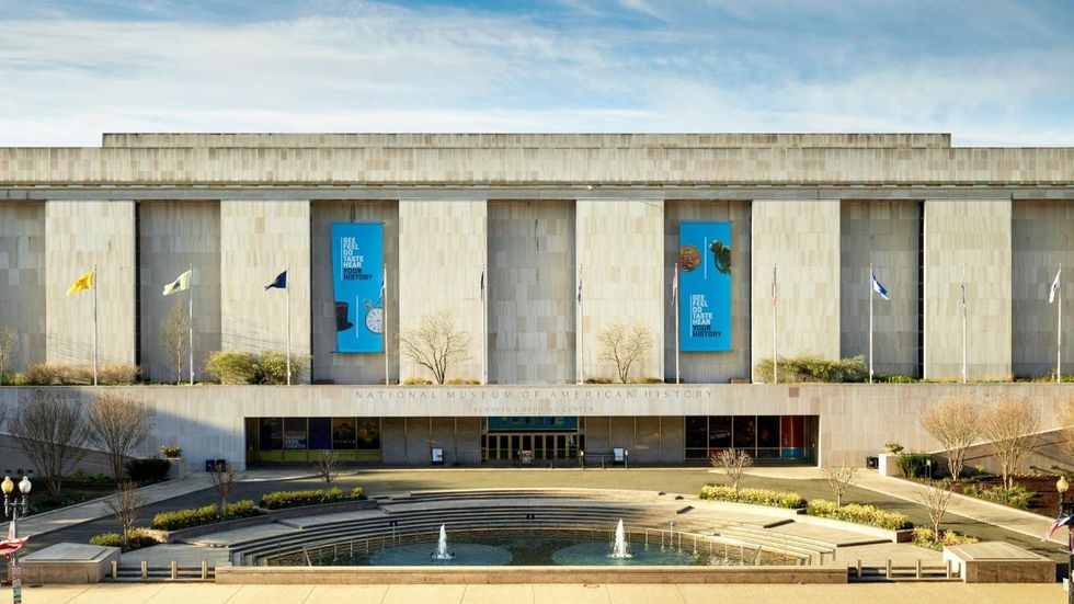 Facade of the Smithsonian's National Museum of American History with flags and banners.