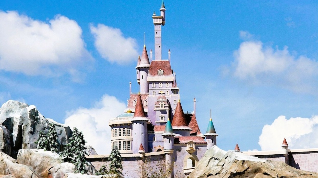 Fairytale castle with red roofs against a blue sky and fluffy clouds.