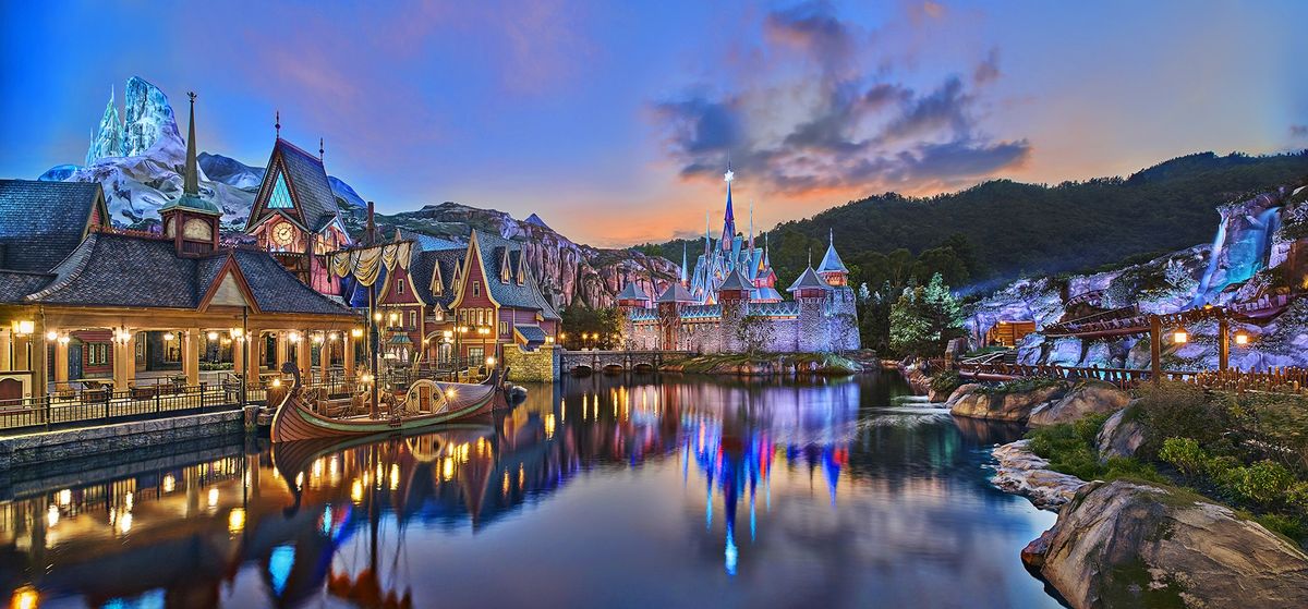 Fairytale village by a serene lake at twilight, with majestic castle and mountain backdrop at Hong Kong Disneyland