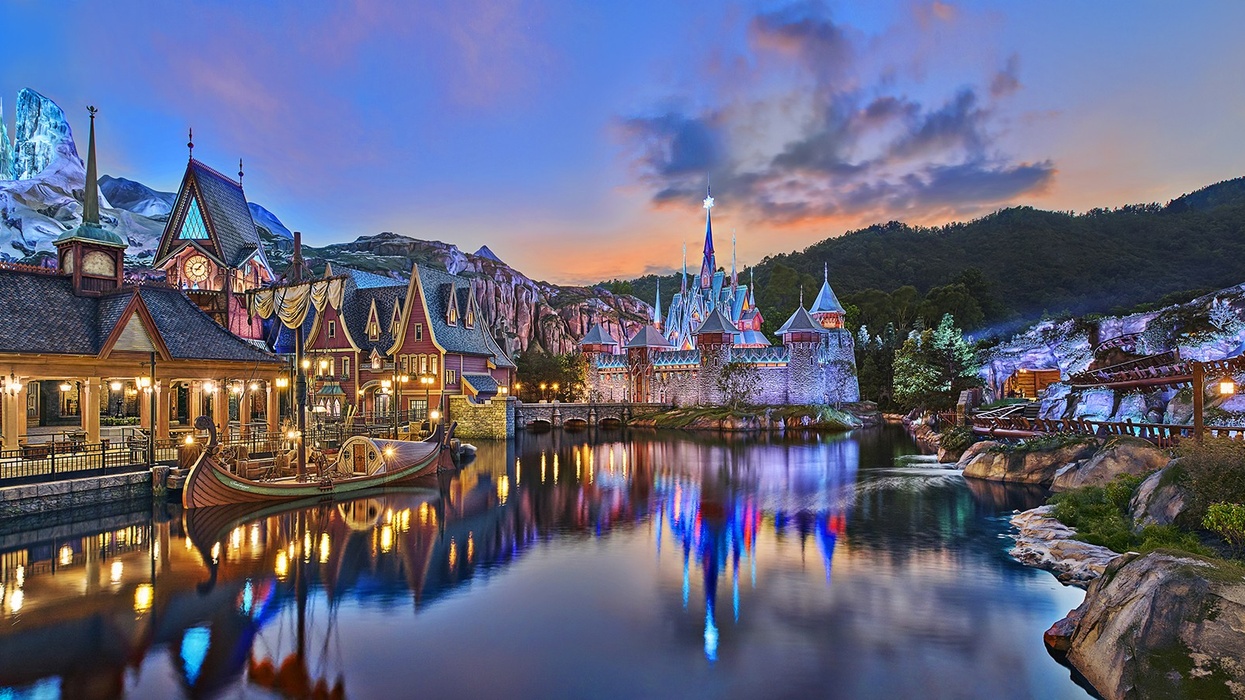Fairytale village by a serene lake at twilight, with majestic castle and mountain backdrop at Hong Kong Disneyland