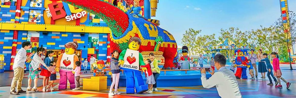 Families enjoying a colorful LEGO park with characters and a large dinosaur sculpture.