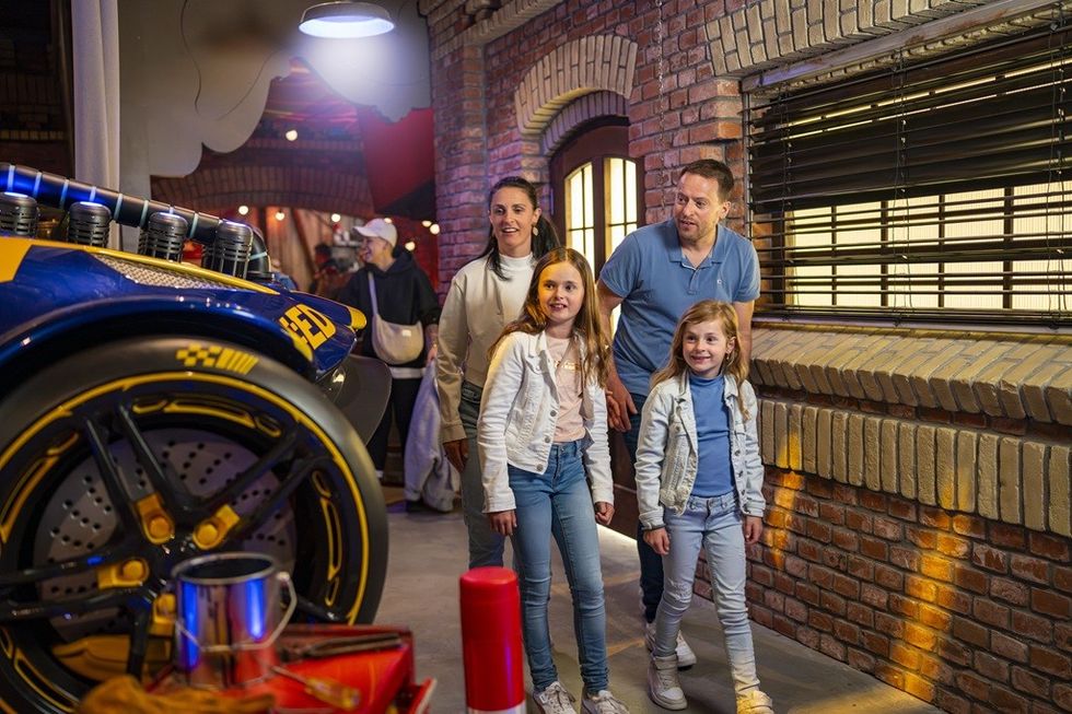 Family admiring a blue and yellow car in a brick-walled exhibition space.