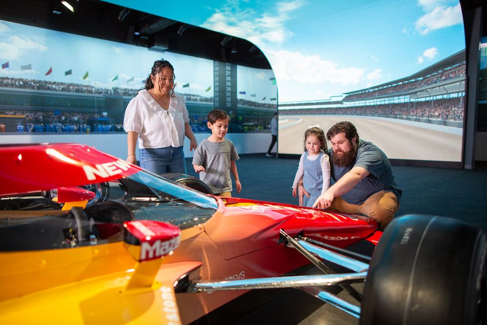 Family admiring an Indy car display with a racetrack backdrop.