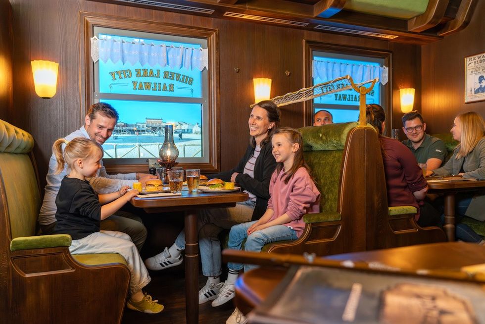 Family dining in a vintage train-themed restaurant, enjoying burgers and drinks.