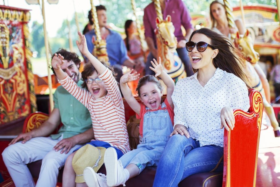 Family enjoying a carousel ride, smiling and raising their hands in excitement.