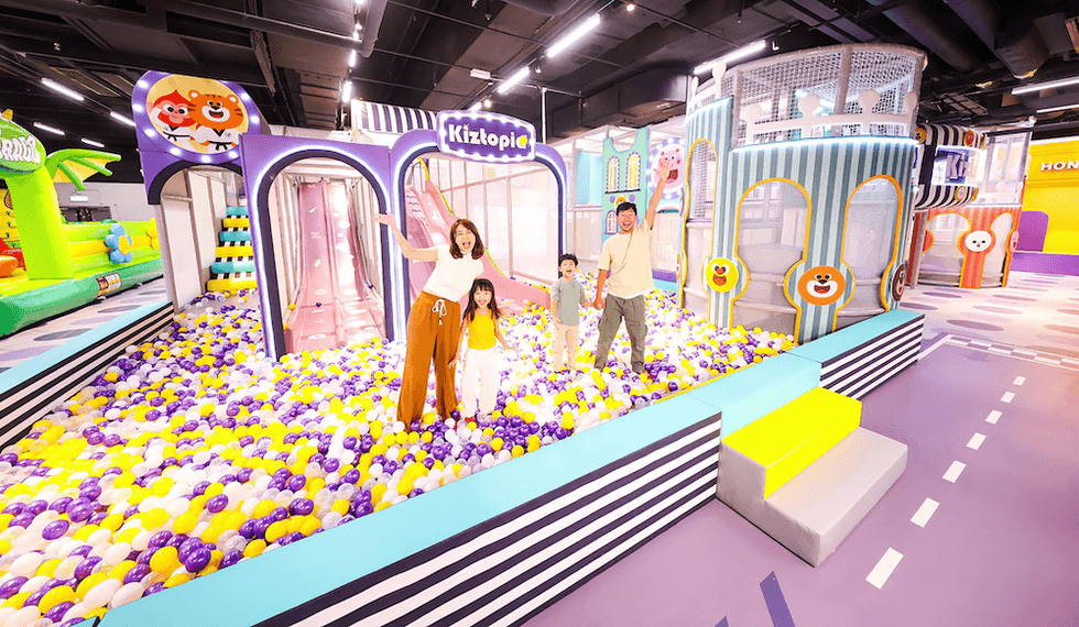 Family enjoying a colorful ball pit in an indoor playground named "Kiztopia."