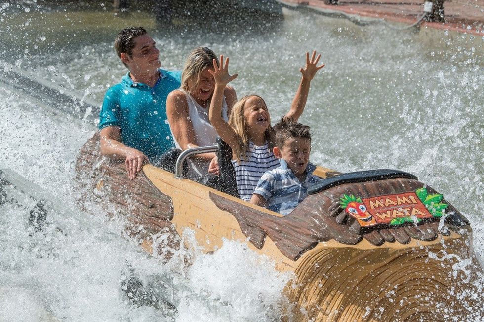 Family enjoying a log ride, splashing through water with arms up in excitement.