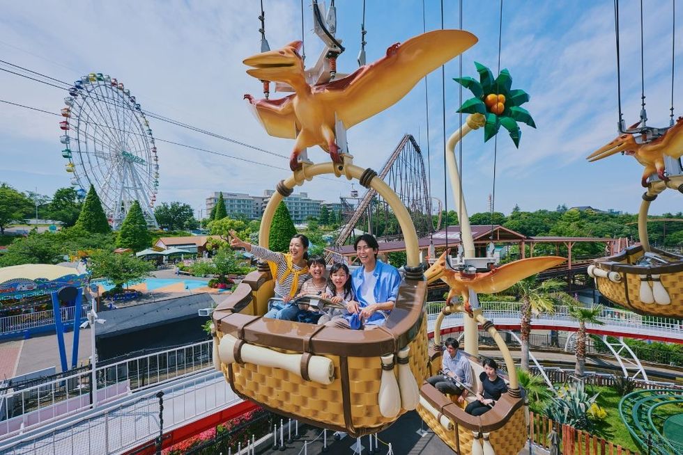 Family enjoying a theme park ride with dinosaur theme; ferris wheel in background.