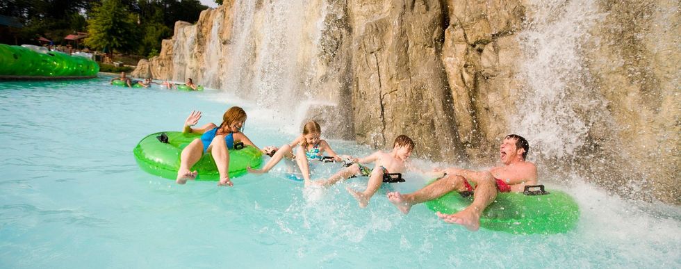 Family enjoying water ride with green tubes under a waterfall at Dollywood's Splash Country
