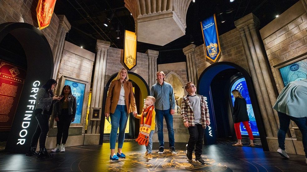 Family exploring a Harry Potter-themed exhibit with Hogwarts house banners.