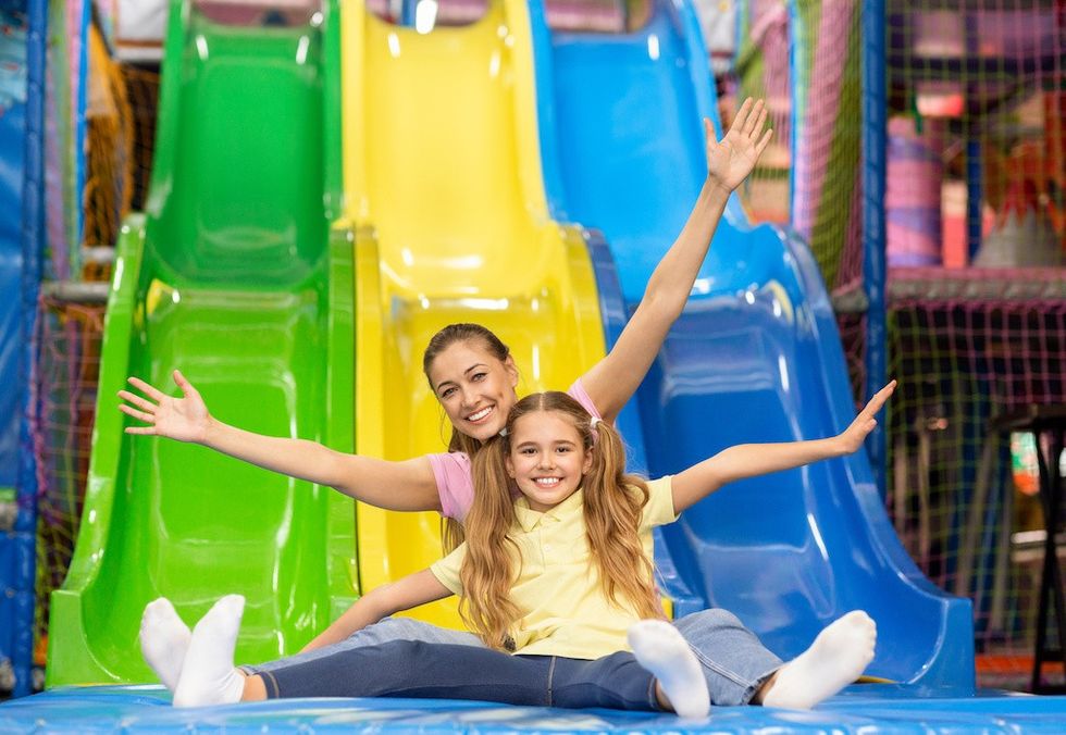 Family fun. Smiling mother and her daughter riding slide together at indoor kids playground