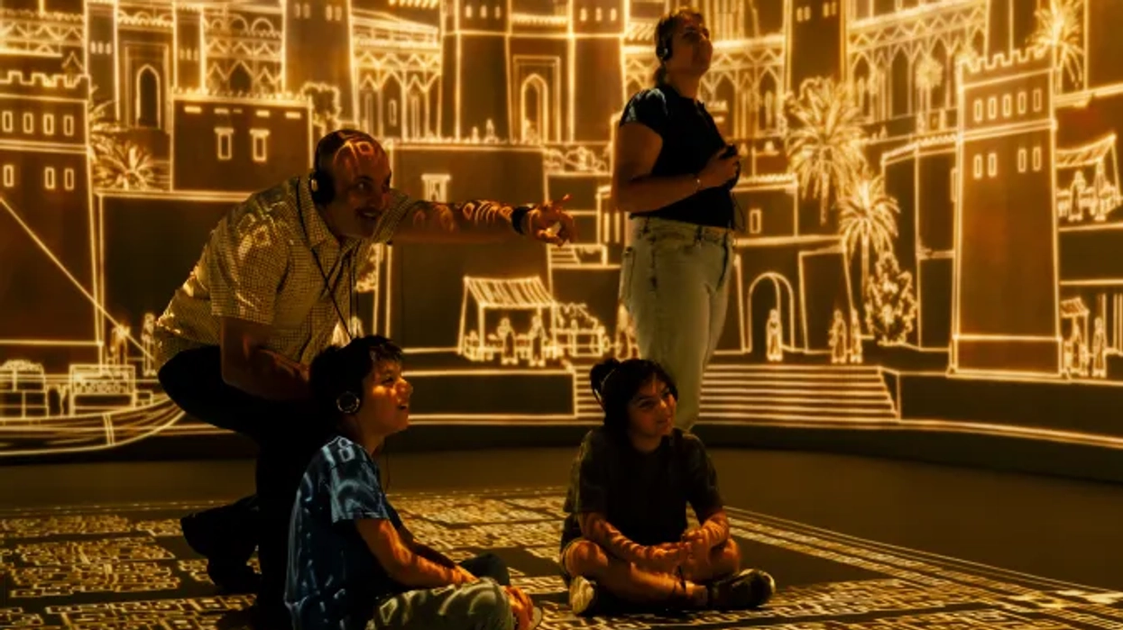 Family observes illuminated cityscape projection in interactive exhibit room.