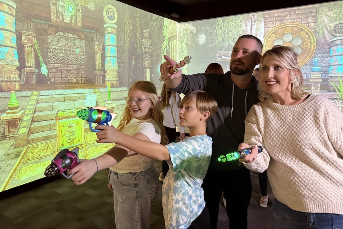 Family playing an interactive FuzionGamz game with light guns in a themed room.
