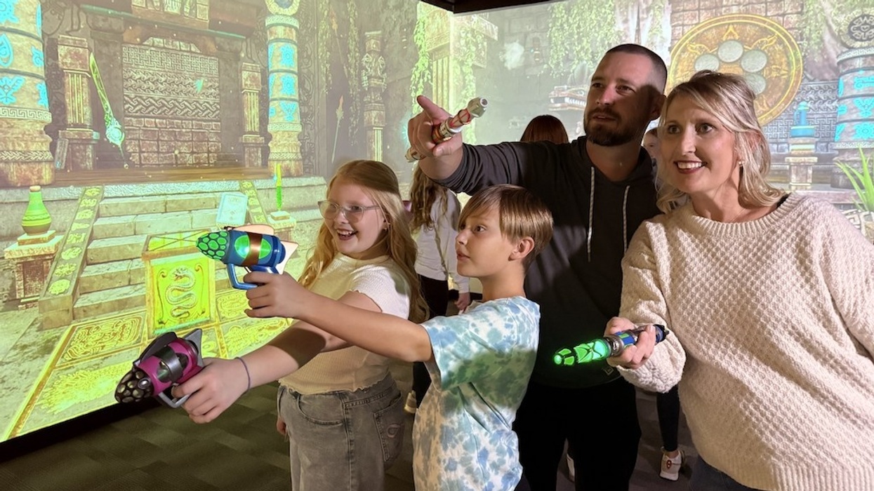 Family playing an interactive FuzionGamz game with light guns in a themed room.