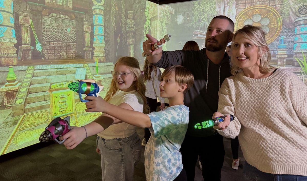 Family playing an interactive game with toy blasters, enjoying an ancient temple backdrop.