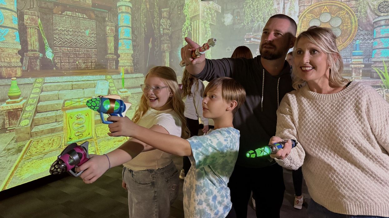 Family playing an interactive game with toy blasters, enjoying an ancient temple backdrop.