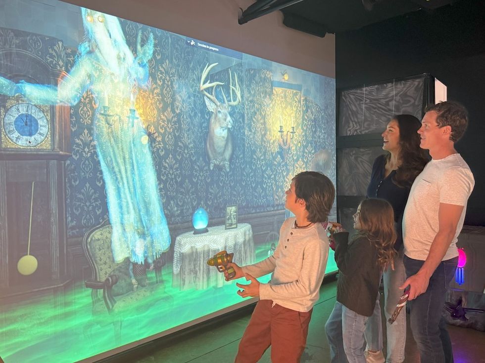 Family playing interactive FuzionGamz game with ghostly figures on a large screen.