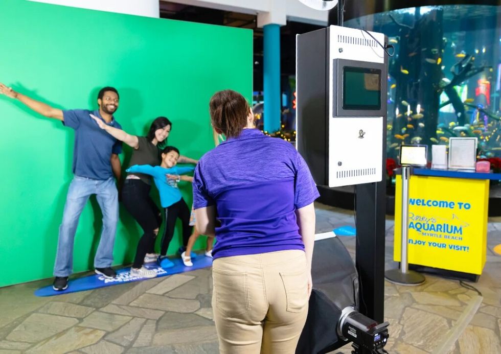 Family posing on surfboard with green screen at an aquarium photo booth.