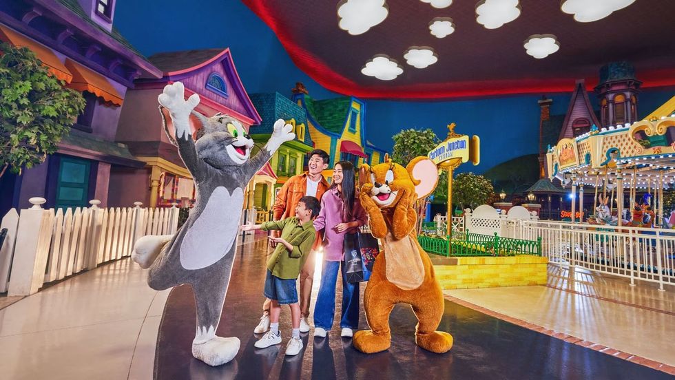 Family posing with Tom and Jerry mascots in a colorful theme park setting at \u200bWarner Bros. World Abu Dhabi